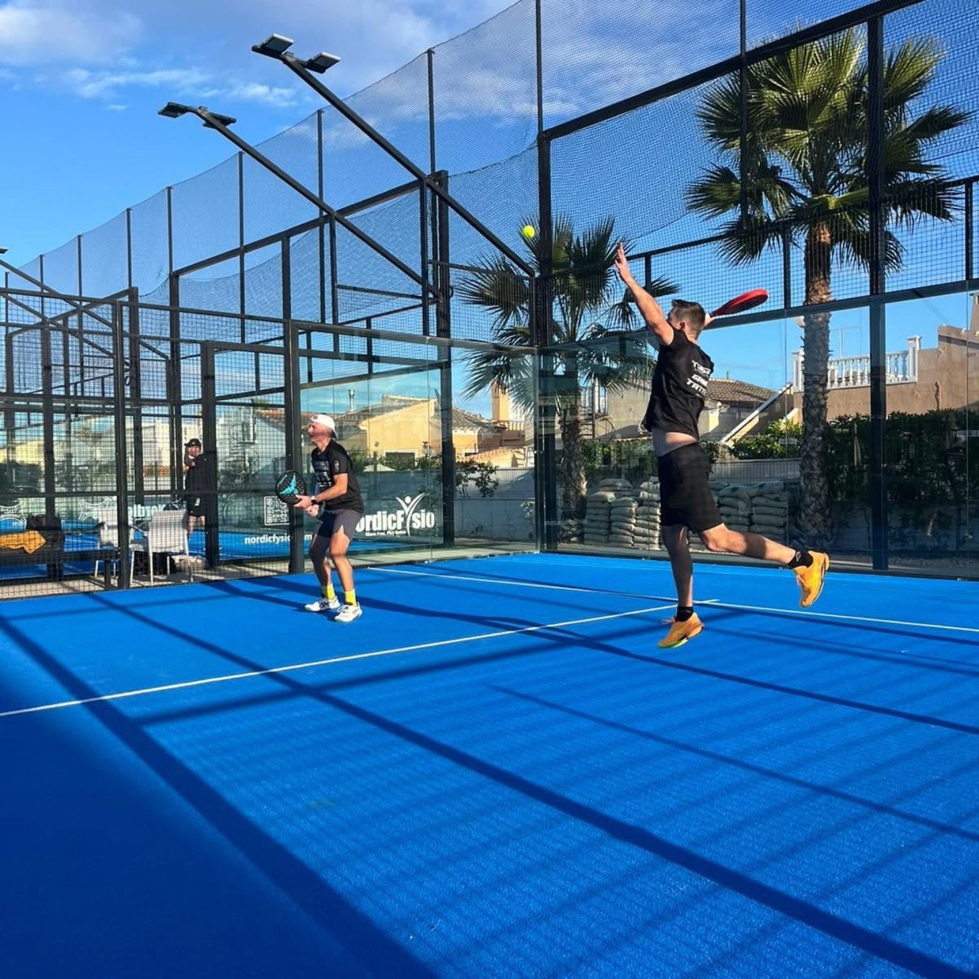 Smash i solnedgång på utomhusbana med palmer